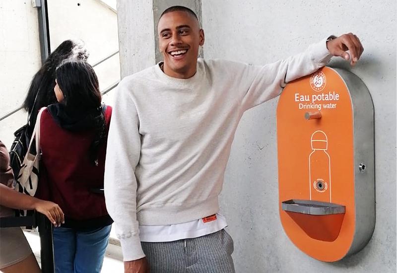 Un homme avec un sweat gris accoudé à une fontaine orange à l'image de roland garros